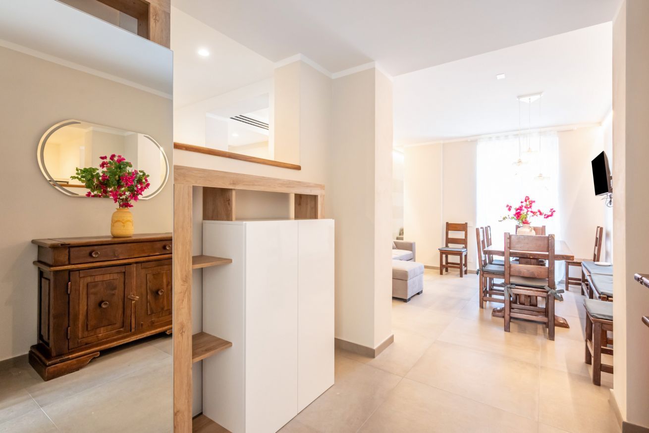 A modern interior with a wooden cabinet, a white shelving unit, and a dining area with wooden chairs and a table.