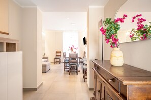 A modern kitchen with a wooden cabinet, a vase with flowers, and a dining area with chairs and a table. - GuestHost - Mare Monti Apartment 7 (Dogana)