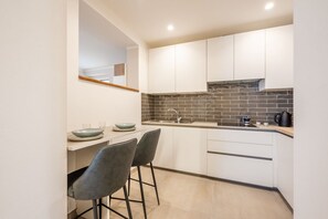 A modern kitchen with white cabinets, a black tiled backsplash, and a built-in stove. There are two bar stools and a small island with a bowl and glasses. - GuestHost - Mare Monti Apartment 7 (Dogana)