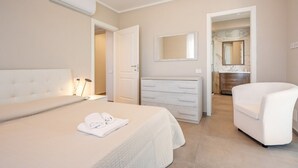 Une chambre à coucher comprenant un lit, une commode, une chaise, un miroir et une salle de bain visible à travers une porte ouverte.