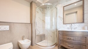 Une salle de bain moderne dotée d’une douche à parois de verre, d’un bidet, de toilettes et d’un meuble-lavabo avec un miroir.