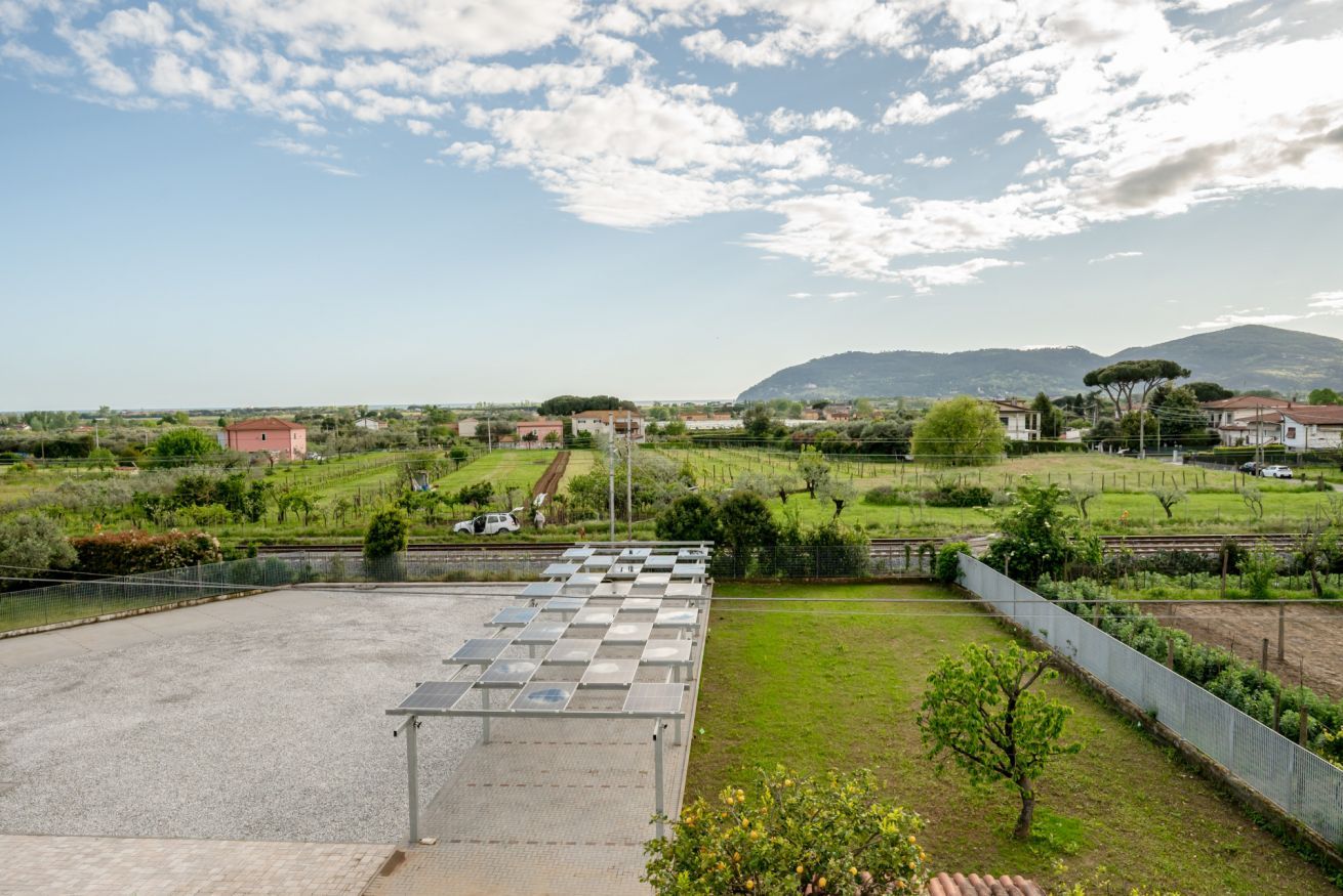 Eine Dachterrasse mit Solaranlagen, einem befestigten Bereich und Blick auf eine ländliche Landschaft mit Häusern und Grünflächen.