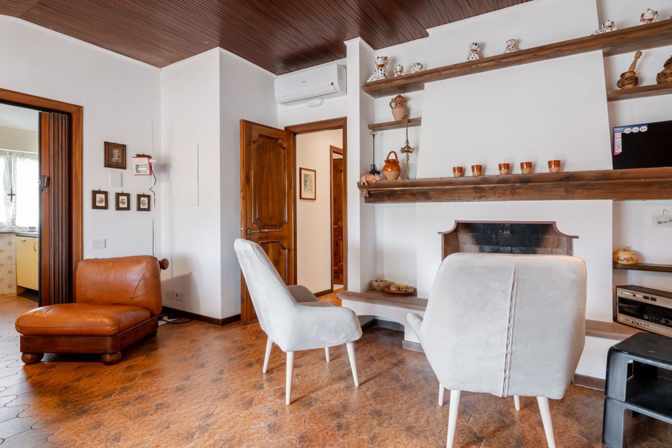 Una sala de estar con chimenea, un sillón de cuero marrón, un sillón blanco y un televisor.