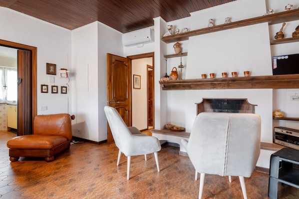 Una sala de estar con chimenea, un sillón de cuero marrón, un sillón blanco y un televisor.