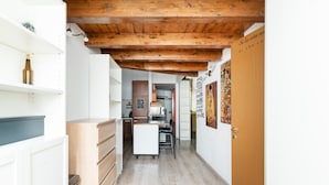 Un couloir étroit avec un plafond en bois, un coin cuisine avec un réfrigérateur blanc et une porte sur laquelle est apposée une pancarte.