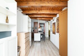 A narrow hallway with a wooden ceiling, a kitchen area with a white refrigerator, and a door with a sign.
