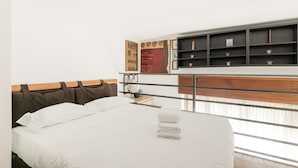 Une chambre à coucher avec un lit, une tête de lit en bois, une étagère fixée au mur ornée d’objets décoratifs et une fenêtre.