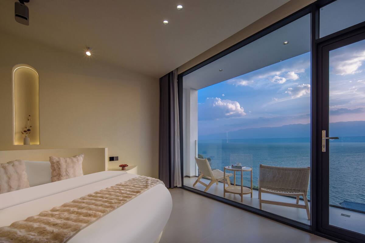 Ein modernes Hotelzimmer mit einem großen Bett, Meerblick und einem Balkon mit Sitzgelegenheit.