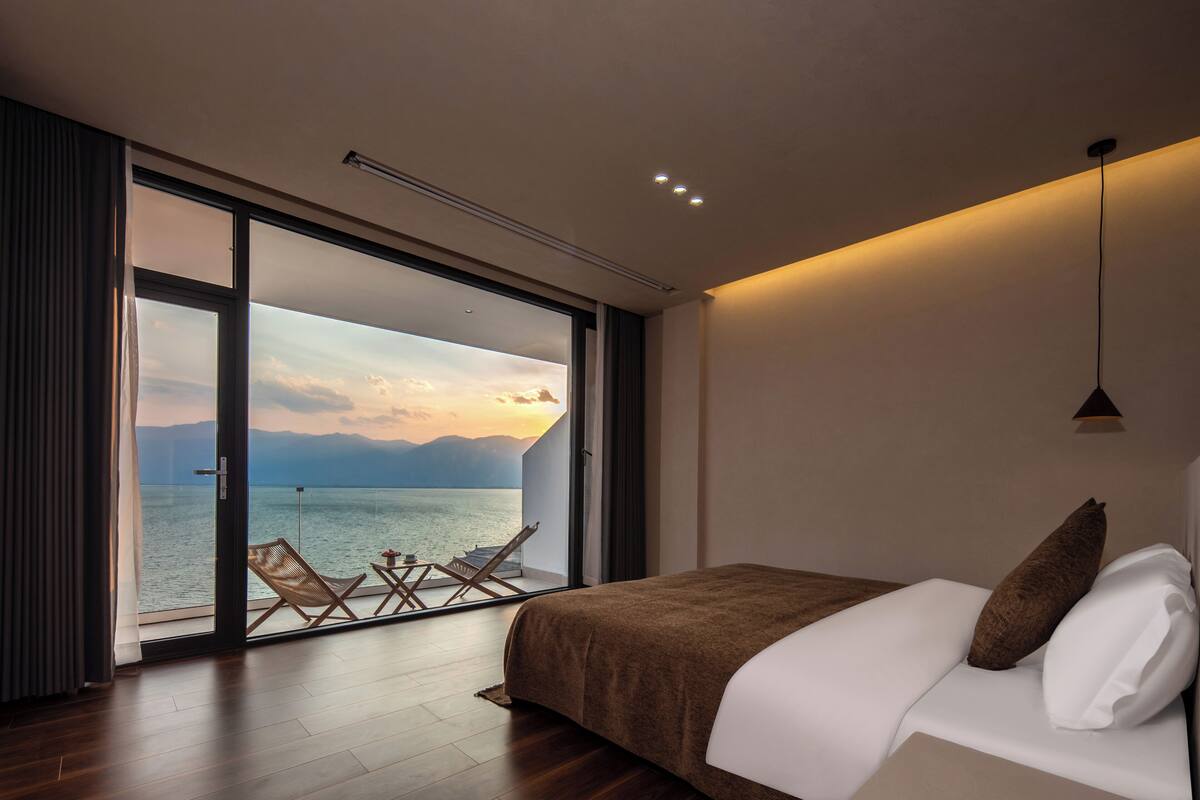 Ein Schlafzimmer mit einer großen Schiebetür, die auf einen Balkon mit Blick auf ein Gewässer und Berge führt.