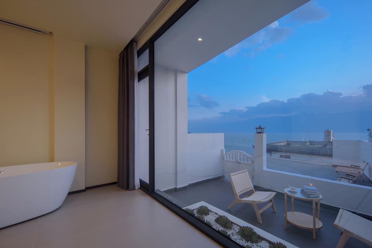Ein modernes Badezimmer mit einer freistehenden Badewanne und einem Balkon mit Sitzgelegenheit und Meerblick.