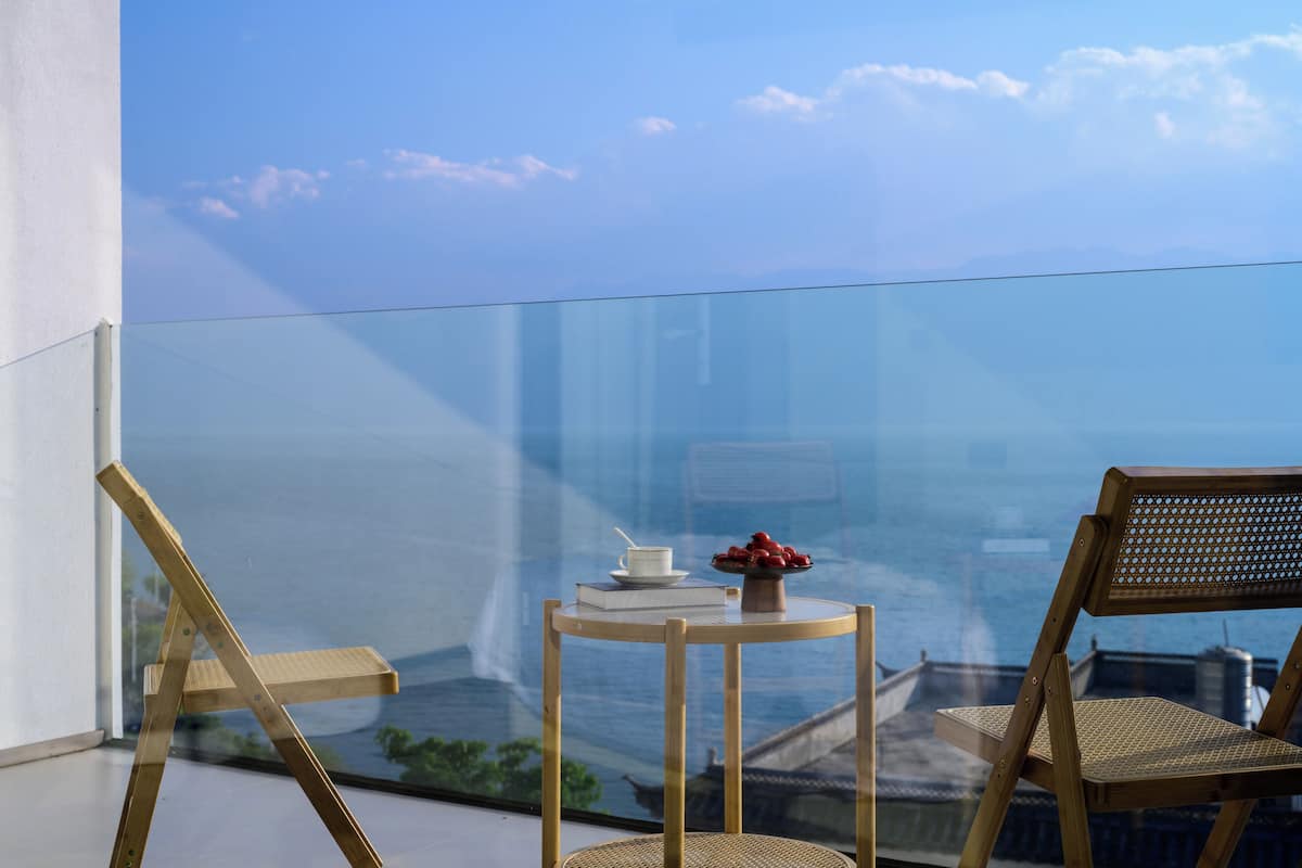 Ein Balkon mit Glasgeländer, ein Holzstuhl, ein kleiner runder Tisch und Blick auf eine Stadtansicht.