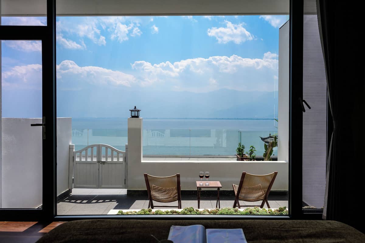 Ein Balkon mit zwei Korbstühlen, einem kleinen Tisch und Blick auf das Meer und entfernte Gebäude.