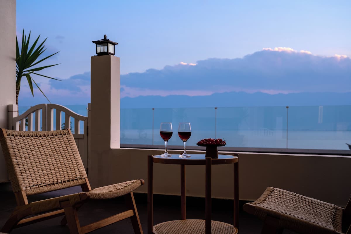 Ein Balkon mit Korbstühlen, einem kleinen Tisch mit zwei Weingläsern und Blick aufs Meer.