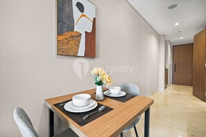 A hotel room with a dining area featuring a wooden table, white plates, and a vase with flowers. - Shika by Kozystay - TB Simatupang (Jakarta)
