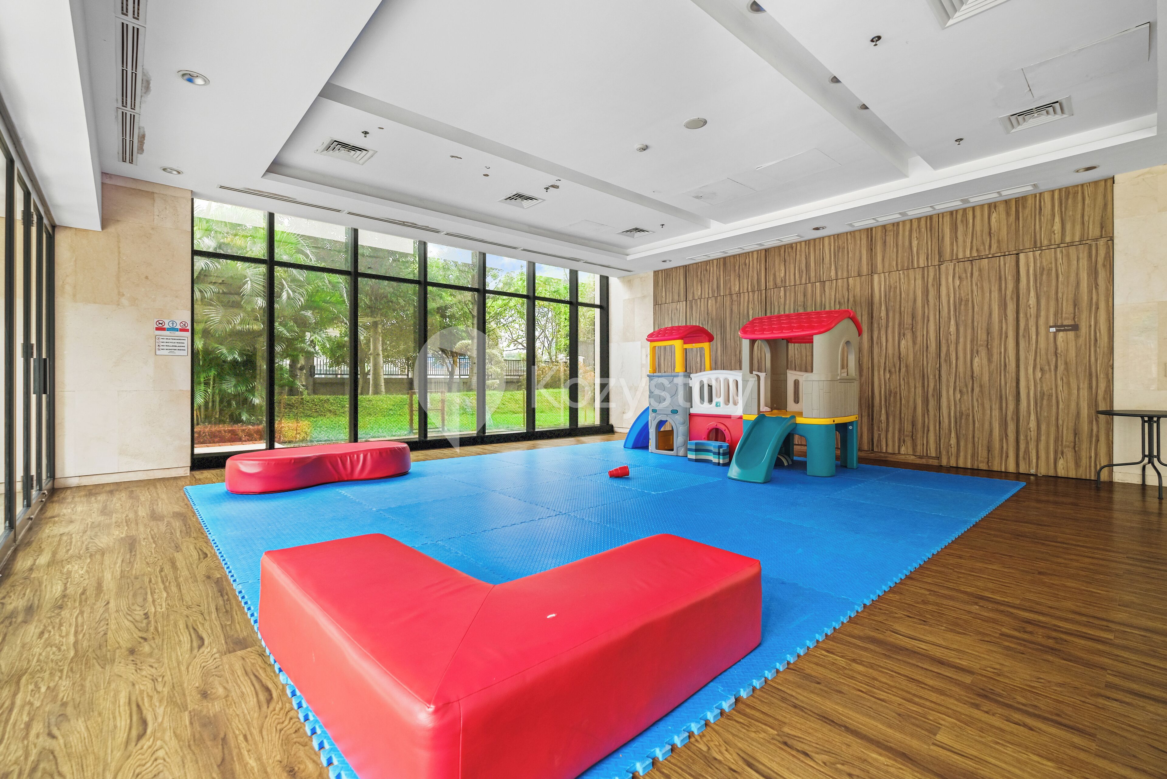Ein großzügiger Indoor-Spielbereich mit blau gepolstertem Boden, Holzwänden und großen Fenstern.
