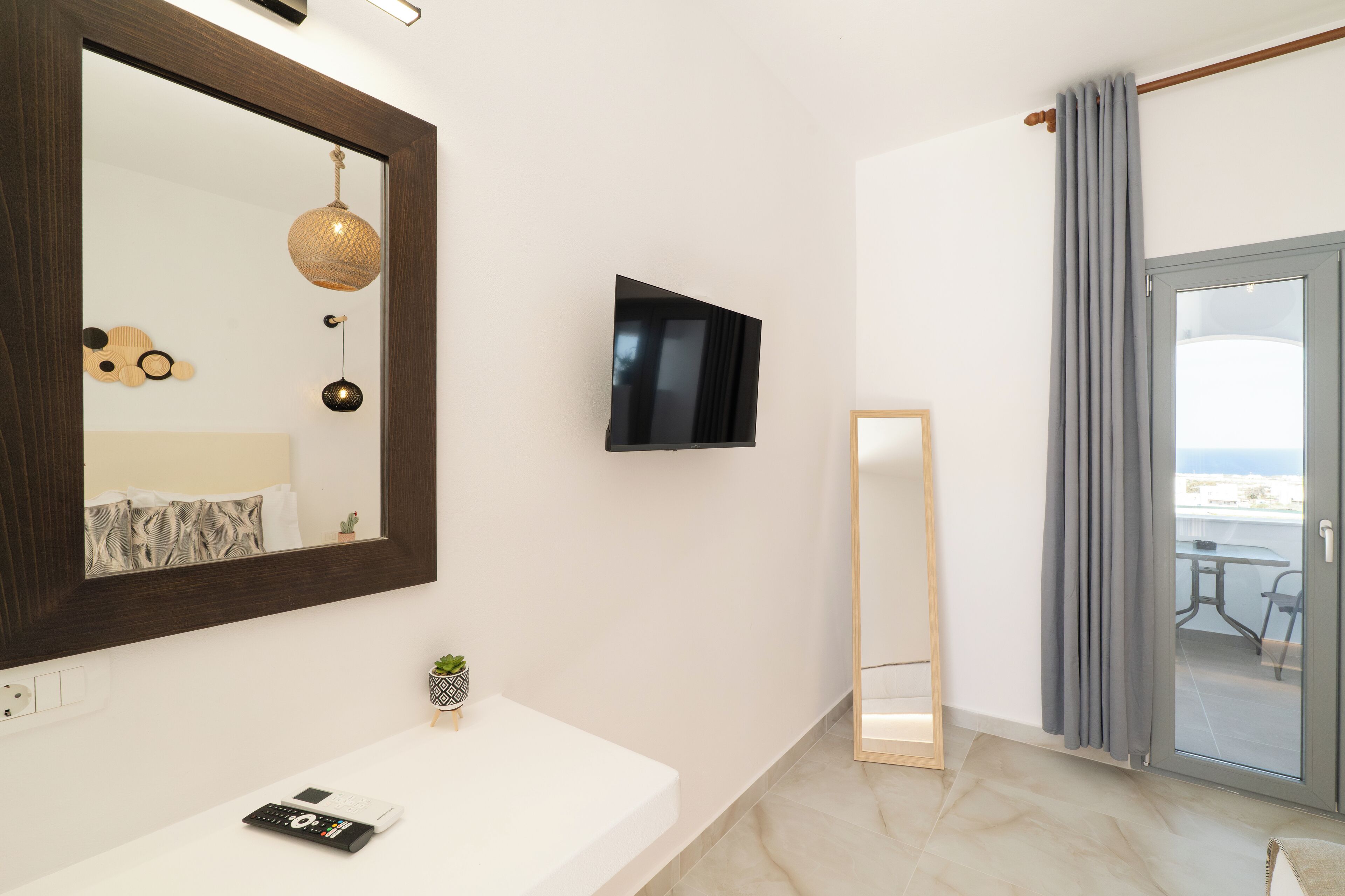 A modern bathroom with a large mirror, a mounted TV, and a sliding glass door to a balcony.