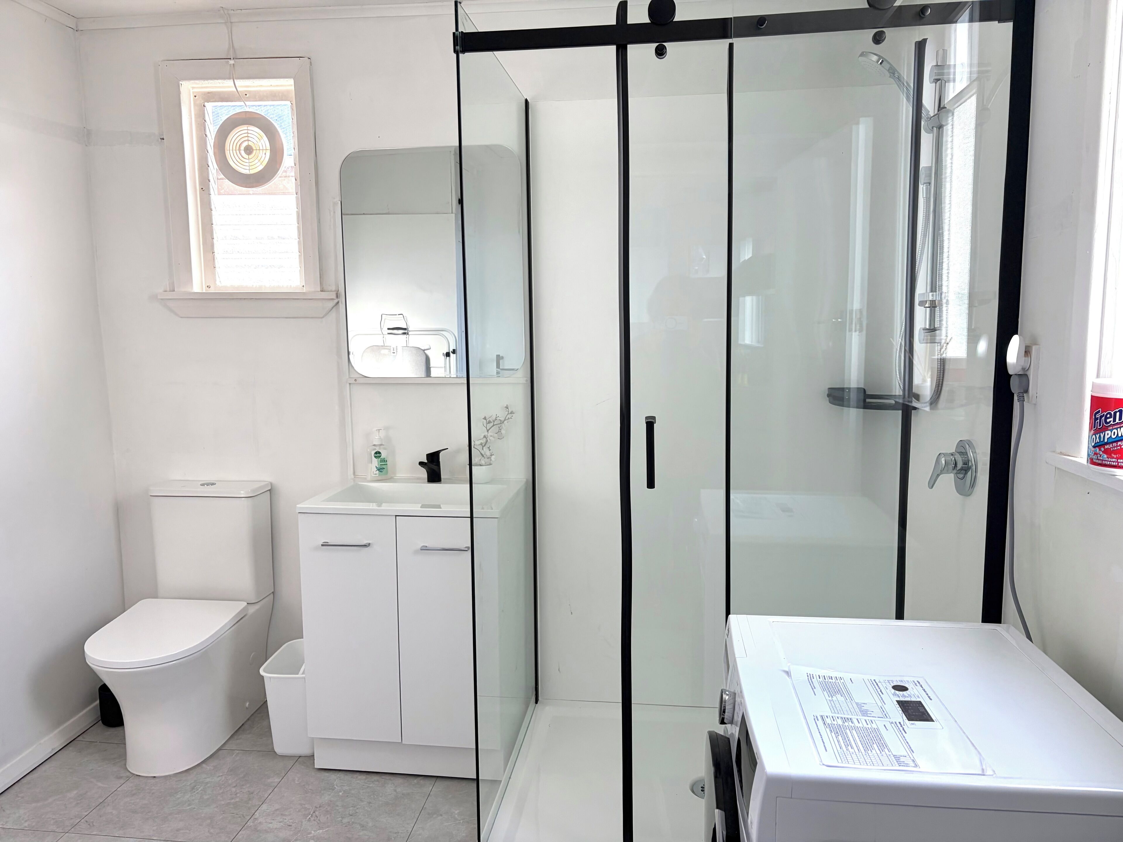 A modern bathroom with a toilet, a sink with a mirror, a shower enclosure, and a white cabinet.