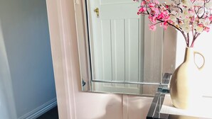 Ein Badezimmer mit Toilette, rundem Hocker, Spiegel und einer Vase mit rosafarbenen Blumen.