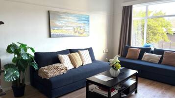A living room with a dark blue sofa, a coffee table with a vase of flowers, and a large window with curtains.