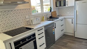 Eine moderne Küche mit weißen Schränken, einer schwarzen Induktionskochplatte, einem eingebauten Backofen, einem Geschirrspüler und einer Edelstahl-Dunstabzugshaube.