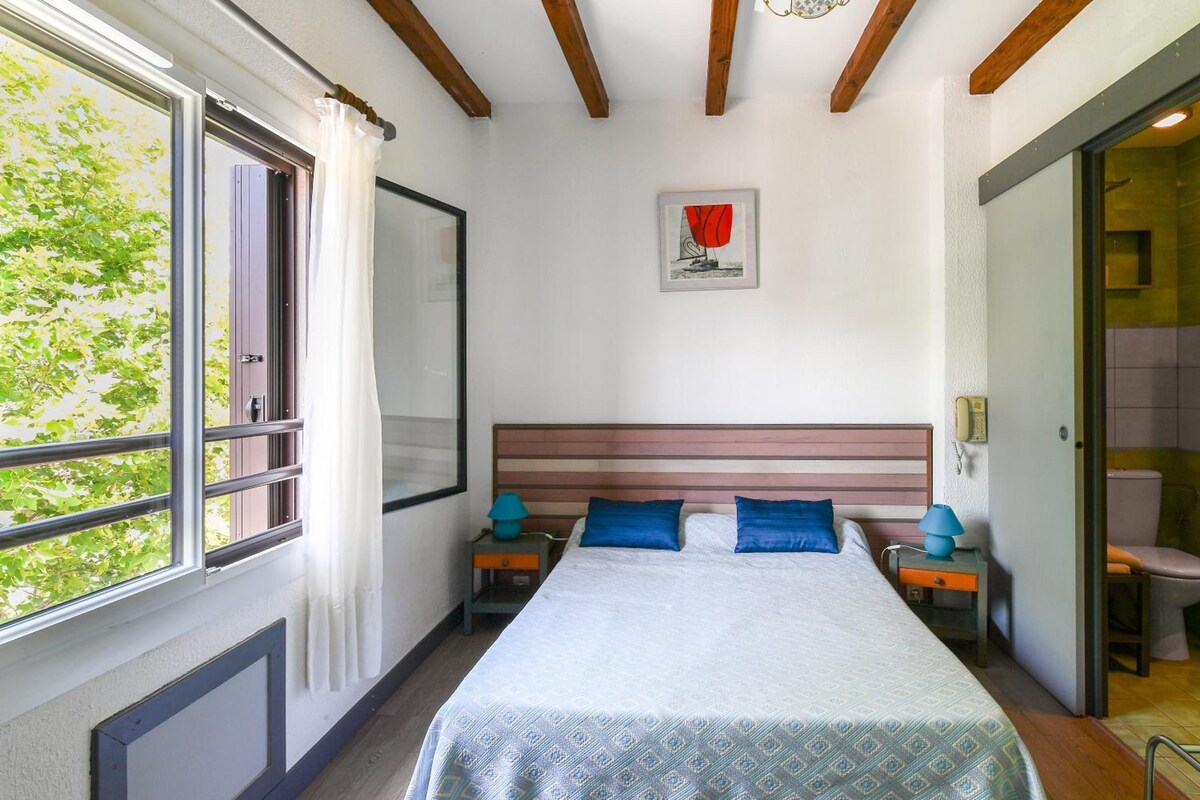 A bedroom with a bed, two nightstands, a painting, and a window with curtains.