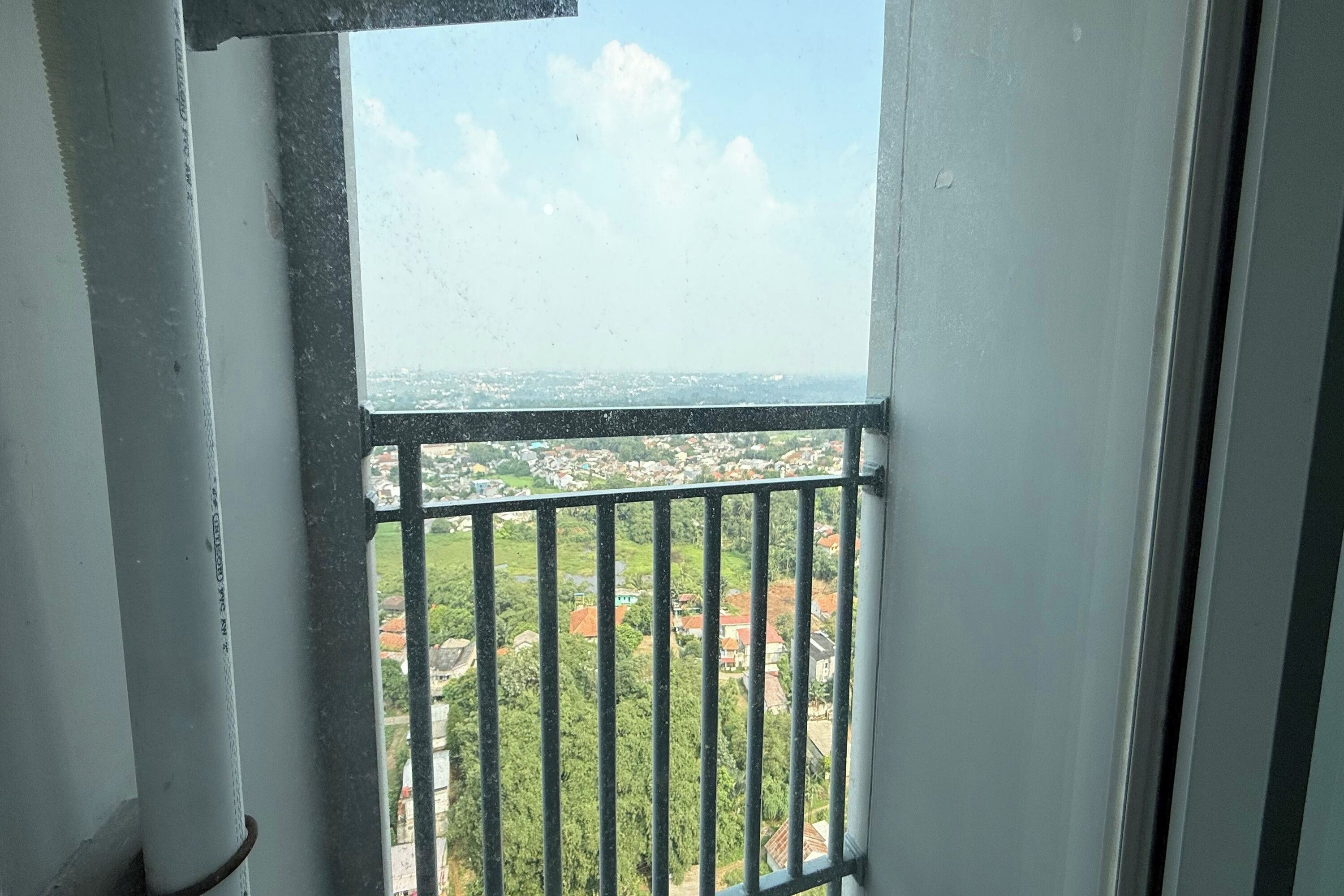 A balcony with a metal railing overlooking a residential area with houses and greenery.