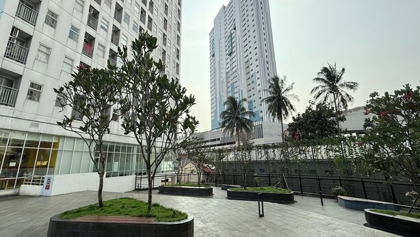 A modern urban plaza with tall residential buildings, landscaped areas with trees, and a glass building with signage. - Serpong Garden NATURE INN (Cisauk)