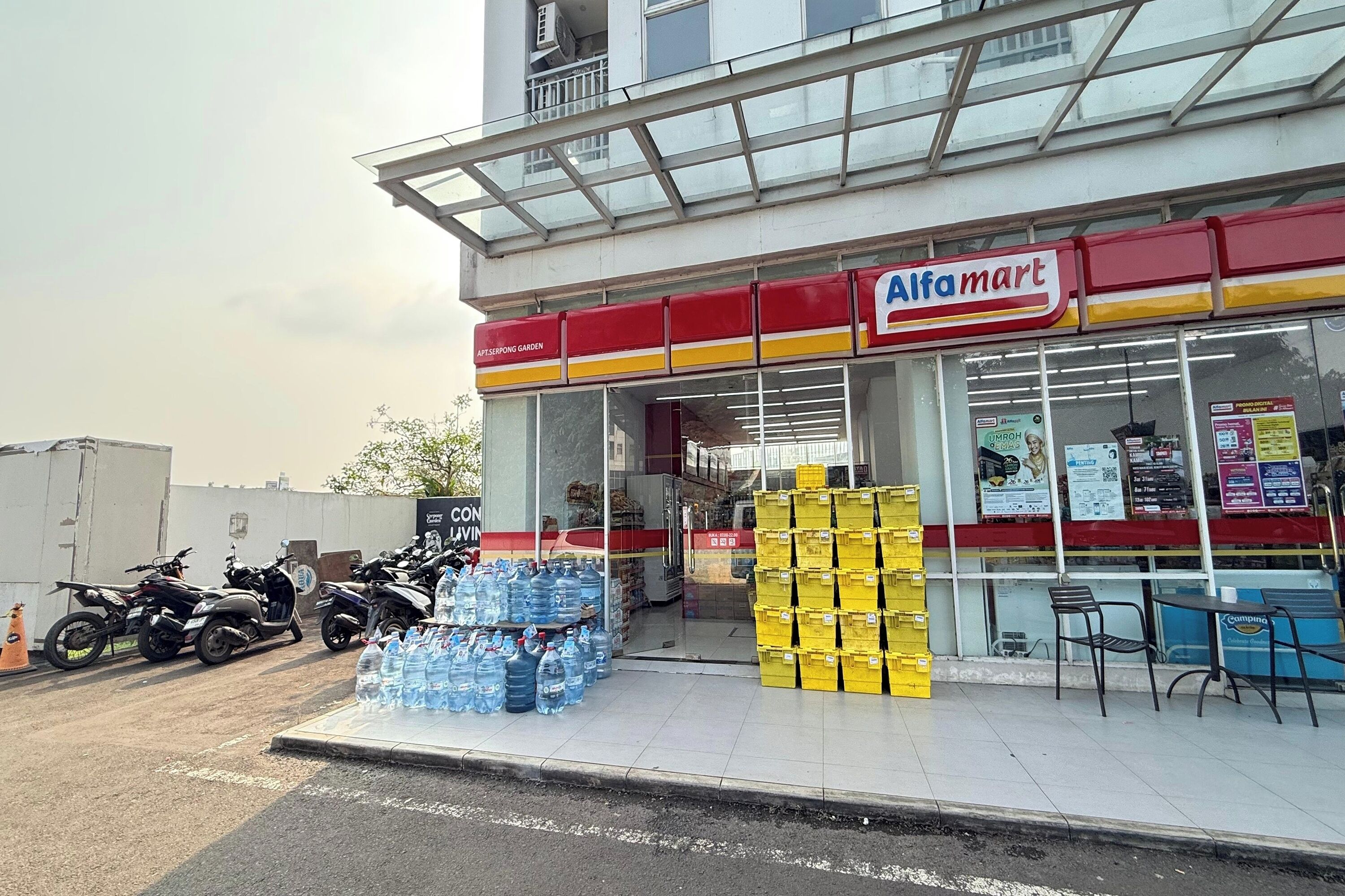 A storefront with a large sign for Alfamart, water bottles stacked outside, and a few motorcycles parked nearby.