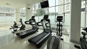 A gym with treadmills, stationary bikes, and a TV screen. - Serpong Garden NATURE INN (Cisauk)
