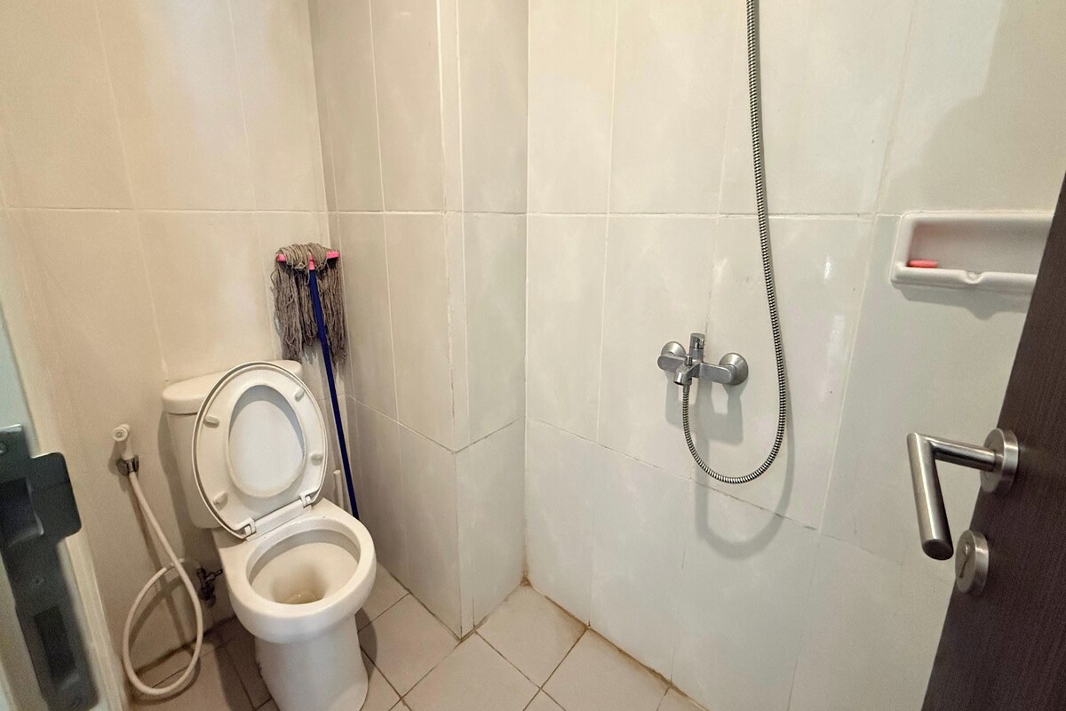 A small bathroom with a toilet, a shower, and a mop.