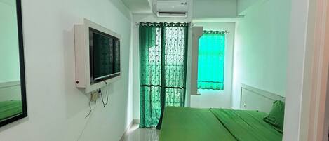 A bedroom with a bed, a TV mounted on the wall, and an air conditioning unit on the ceiling.