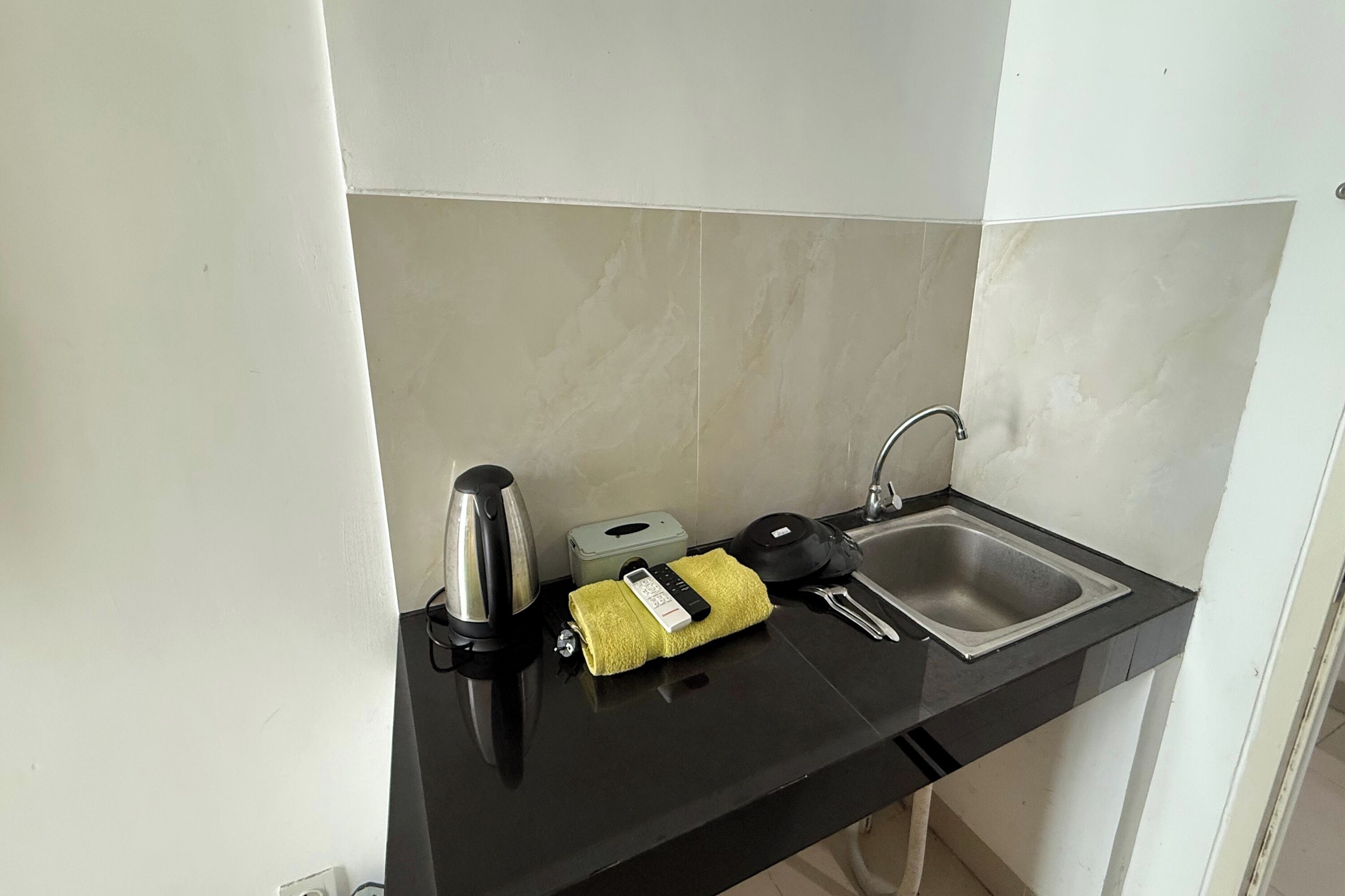 Una piccola cucina con un piano di lavoro nero, un bollitore, un tostapane, un lavandino e un asciugamano.