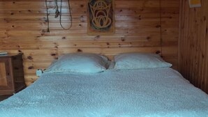 A wooden-paneled room with a bed, a nightstand, and wall-mounted lamps.