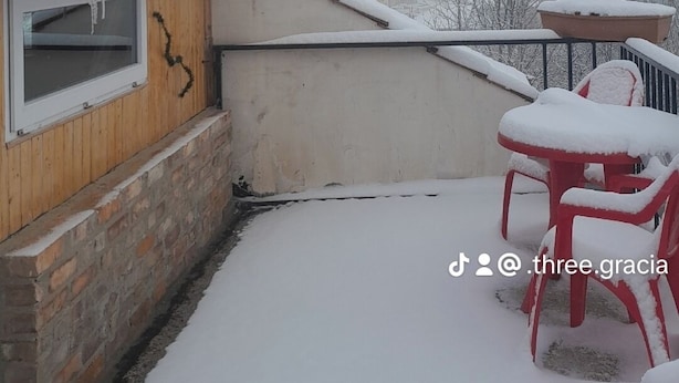 A snow-covered patio with a wooden building, a brick wall, and a red plastic table and chairs.