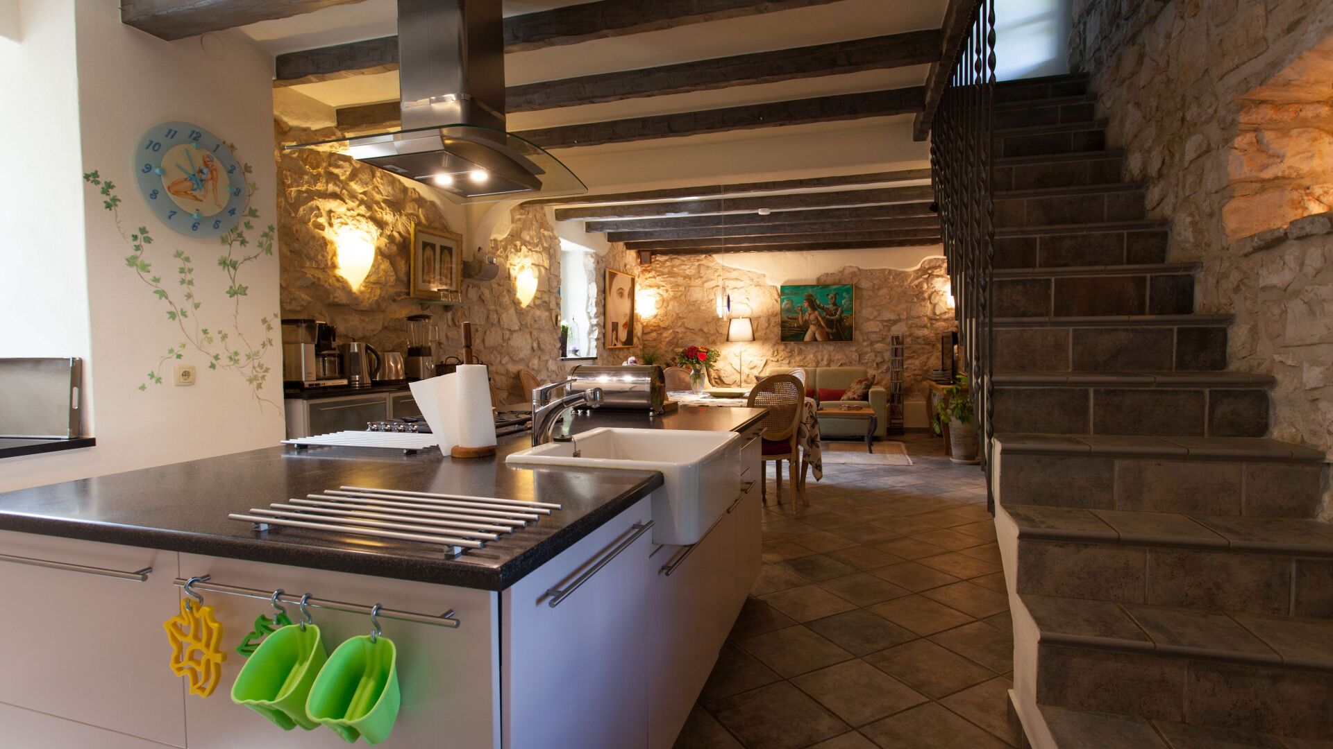 A modern kitchen with a central island, stone walls, and a staircase leading to an upper level.
