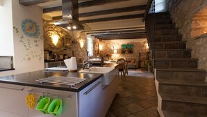 A modern kitchen with a central island, stone walls, and a staircase leading to an upper level.