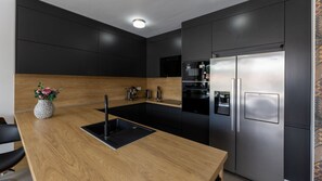 A modern kitchen with a wooden countertop, black cabinets, and a stainless steel refrigerator. - Villa Juma by Villas Guide (Blace)