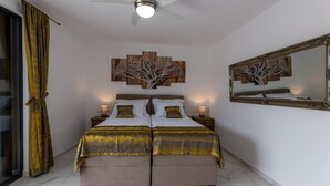 A bedroom with a large bed, two bedside tables, a ceiling fan, a wall-mounted mirror, and a tree-themed artwork above the bed. - Villa Juma by Villas Guide (Blace)