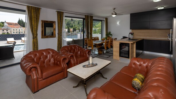 A modern living room with leather sofas, a dining area, and a kitchen. - Villa Juma by Villas Guide (Blace)