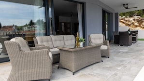 A modern outdoor living area with wicker furniture, a glass-top coffee table, and a view of the surrounding landscape. - Villa Juma by Villas Guide (Blace)