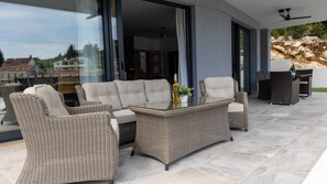 Un espacio al aire libre moderno con mobiliario de mimbre, una mesa de centro de cristal y vistas del paisaje circundante.