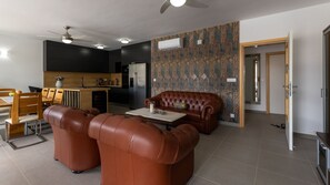 A modern living room with a brown leather sofa, a dining area with wooden furniture, and a kitchen with dark cabinetry. - Villa Juma by Villas Guide (Blace)