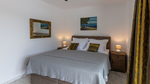 A bedroom with a bed, two bedside tables, a nightstand, a mirror, and two paintings on the wall. - Villa Juma by Villas Guide (Blace)