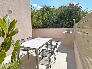 Een terras buiten met een tafel, stoelen, een kleine barbecue en uitzicht op bomen.