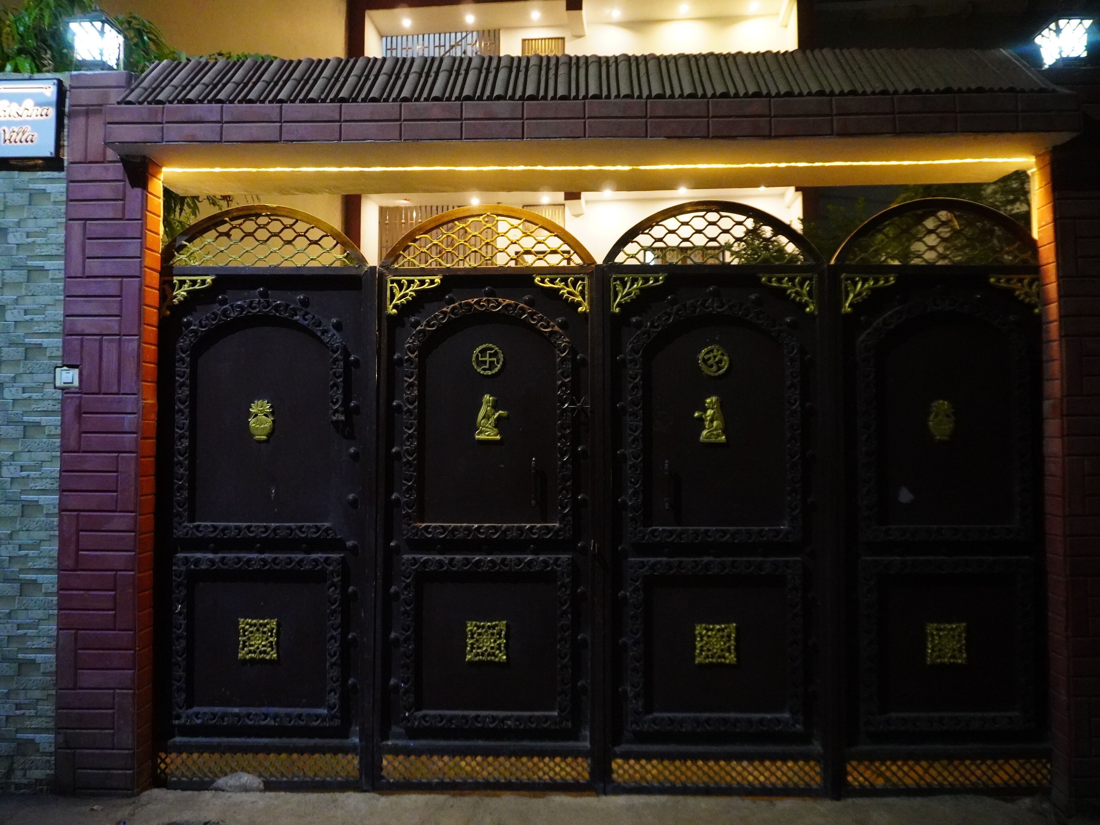 A set of ornate black gates with golden accents and symbols, leading to a building with a tiled roof.