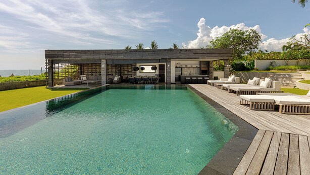 A modern pool area with a wooden deck, lounge chairs, and a bar area with a view of the ocean.