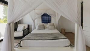 A bedroom with a canopy bed, a view of the outdoors, and a patterned wall hanging.