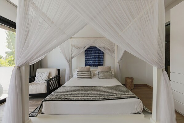 A bedroom with a canopy bed, a view of the outdoors, and a patterned wall hanging.