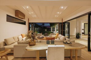 A modern living room with a large sofa set, a wooden coffee table, and a view of the outdoor garden at dusk.