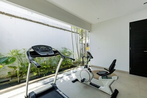 A home gym with a treadmill and an elliptical machine, large windows, and a view of a garden.